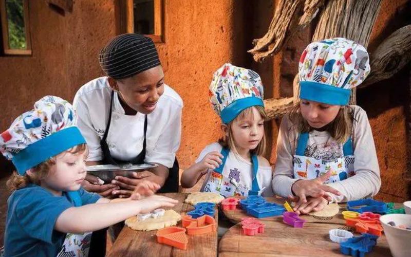 Children enjoy a fun cooking class at a family-friendly safari lodge in South Africa, guided by a chef. Is South Africa safe for kids? With experiences like this, families can explore safely.