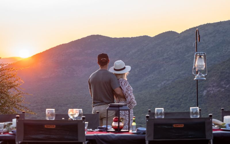 Couple enjoying a romantic sunset dinner at a luxury game lodge in South Africa, overlooking the wilderness during an intimate safari experience.