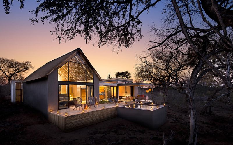 Luxury safari villa at sunset with warm ambient lighting, private plunge pool, and modern thatched architecture surrounded by African bushveld.