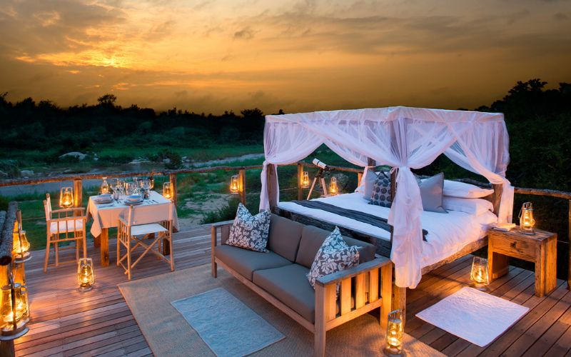 Luxury safari sleep-out deck at sunset with lanterns and a four-poster bed, highlighting experiential stays shaping today’s luxury safari trends.